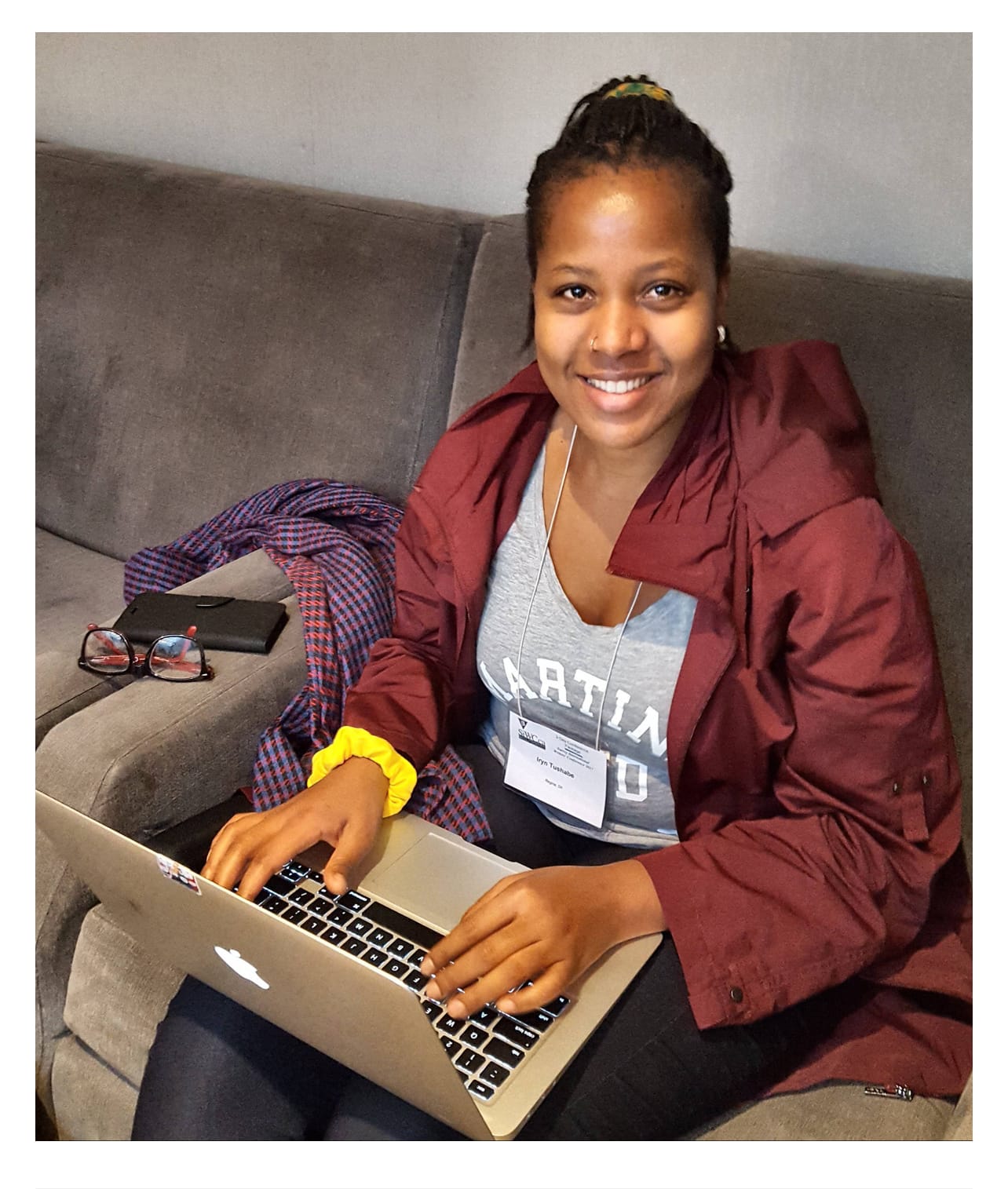 A smiling black woman typing on a laptop that's balancing on her lap